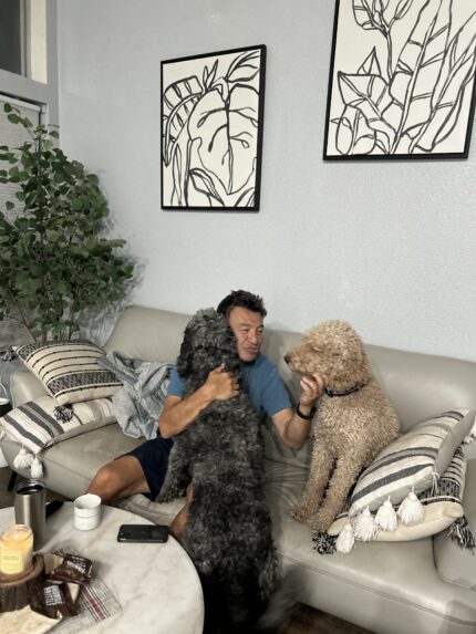 Person sitting on a couch with two dogs, smiling and relaxed.